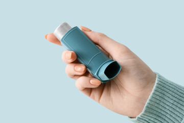 Woman holding asthma inhaler on blue background, closeup