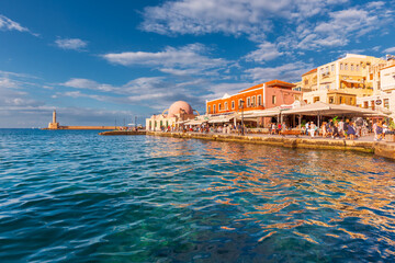 Old town seafront with cafes, houses, colorful reflection in water and lighthouse, Chania, Greece