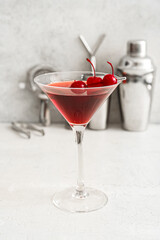 Glass of tasty Manhattan cocktail with cherries on light background