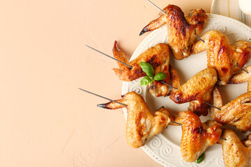 Plate with grilled chicken wings skewers on beige background, closeup