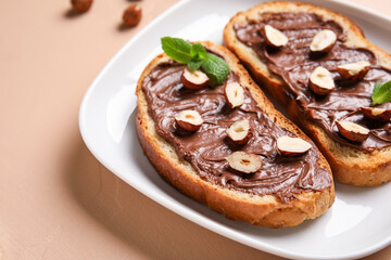 Plate of bread with chocolate paste and hazelnuts on beige background, closeup
