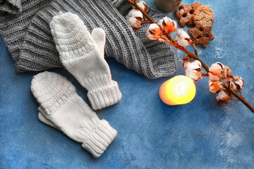 Warm gloves, scarf and burning candle on blue background