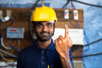 Focus on hand, Electrical engineer with hard hat at work place showing voted ink finger by looking...