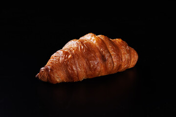 One croissant lies on a black matte background.