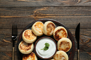 Plate with tasty cottage cheese pancakes and sauce on wooden background
