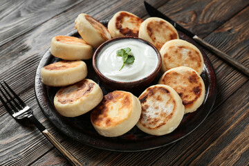 Plate with tasty cottage cheese pancakes and sauce on wooden background, closeup