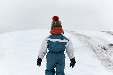 Back view the child walks in the winter on the street. Boy walks on loose snow. Cold winter day.