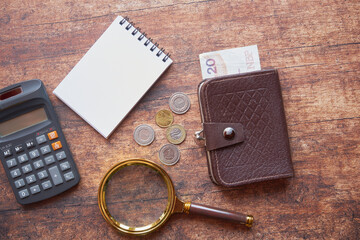notes, monety, kalkulator ,lupa i brązowy portfel na drewnianym stole ,polski złoty 
