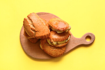 Wooden board of tasty sochniki with cottage cheese on yellow background