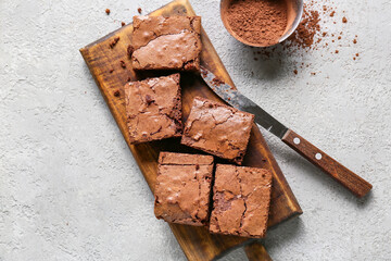 Wooden board with pieces of tasty chocolate brownie on light background