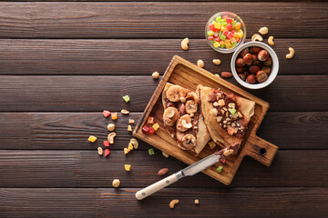 Board of tasty thin pancakes with chocolate paste and nuts on dark wooden background