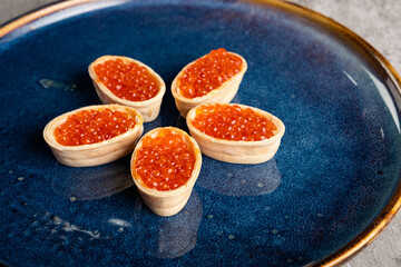 Delicious appetizer Tartlets with red caviar and butter on a blue plate close-up. Horizontal orientation, no people, copy space