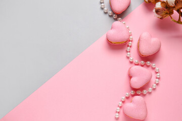 Tasty heart-shaped macaroons and beads on color background