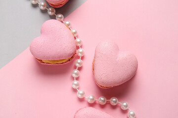 Tasty heart-shaped macaroons and beads on color background