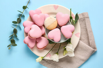 Plate with tasty heart-shaped macaroons and flowers on blue background