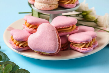Plate with tasty heart-shaped macaroons on blue background, closeup