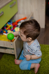 Fototapeta na wymiar child toddler playing toys at home or nursery, baby holds a green ball in his hand 