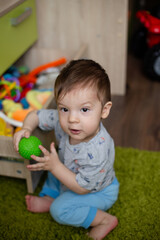 Fototapeta premium child toddler playing toys at home or nursery, baby holds a green ball in his hand