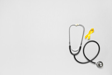 Golden awareness ribbon and stethoscope on light background. International Childhood Cancer Day
