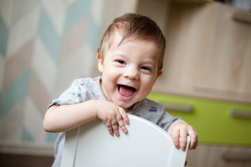 Handsome baby laughs and looks at the camera, baby is holding on to the high chair