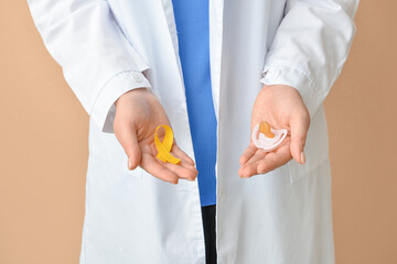 Female doctor holding pacifier and golden awareness ribbon on color background. International...