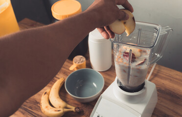 Hand holding an apples, preparation of smoothie with milk, banana and oatmeal.