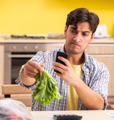 The young man calculating expences for vegetables in kitchen
