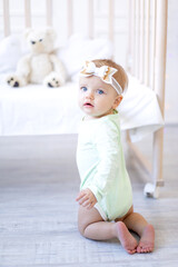 a small child girl stands or climbs on the crib in the nursery in a white cotton bodysuit