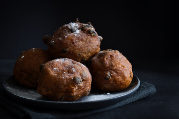 Deep-fried raisins buns. Dutch donuts with raisins and powdered sugar on a plate. Dark moody food photography style with selective focus and copy space, horizontal