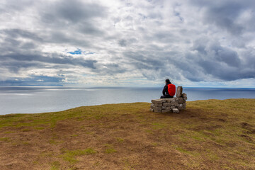 Woman on a bench looking at Leitisvatn Lake, Faroe Islands.