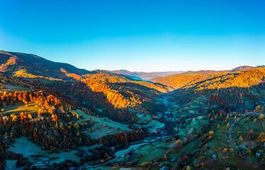 Shaded mountain valley with houses and forests at sunset