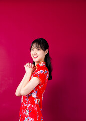 Smiling asian young woman in traditinal red cheongsam dress pointing hand to empty space on red background.