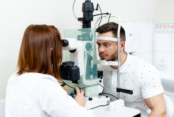 Naklejka na ściany i meble Young optometrist examining patients eyes. Optician specialist eyesight testing.