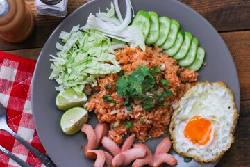 American fried rice is served with sausages, cucumbers, shredded vegetables in a gray plate on a slatted table with seasonings.