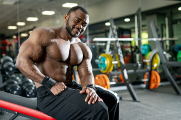 Fototapeta na wymiar Muscular shirtless bodybuilder smiling into camera. Portrait of attractive athletic sportsman in gym.