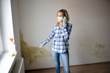 woman standing in front of wall with mold and talking on cell phone and is depressed and frustrated