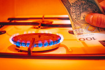 A lit gas stove with a Polish banknote of PLN 100 in hand, Concept of gas increases in Poland in...