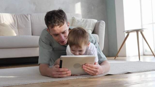 Happy father and cute preschool son using tablet watching cartoon enjoying watching funny social media video shopping online relaxing at home together