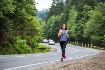 Runner woman running on the mountain road through the forest. Female sport girl training outdoors for marathon