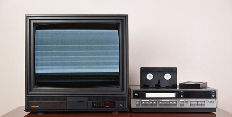 Old analog TV with noise on the screen and VCR. Old black TV with VCR on wallpaper background. 