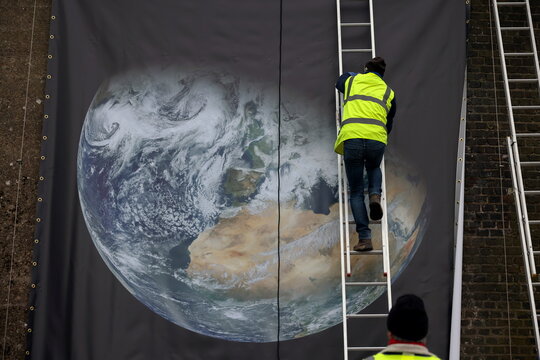 Members of Abundance London install a NASA public domain image of the planet on the railway embankment in Chiswick