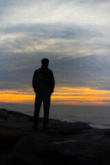 Beautiful sunset on the seashore. A man standing with a backpack on a rock by the sea against a colorful sunset sky.