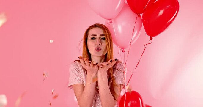 Beautiful redhead girl with red heart balloon posing. Happy Valentine's Day concept. Studio photo of beautiful ginger girl dancing on pink background.