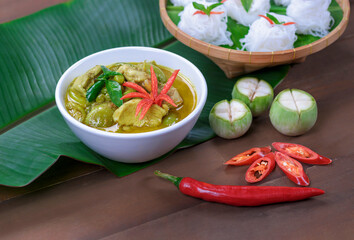 Chicken green curry in white ceramic bowl with rice noodles on wooden table decorations in vintage style