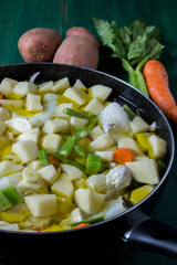 Boiled cod with potatoes, celery and carrots. Close-up of pan ready to cook, on green wooden background