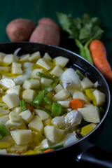 Boiled cod with potatoes, celery and carrots. Close-up of pan ready to cook, on green wooden background
