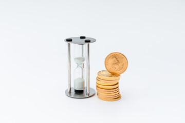 Gold coins stand next to an hourglass