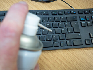 A dusty and dirty black computer keyboard about to be cleaned using a can of pressurized air
