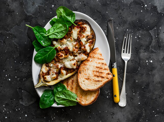 Ratatouille stuffed baked eggplant with mozzarella cheese, spinach and grilled bread on a dark background, top view