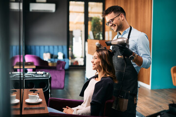 Young happy woman getting her hair styled by male hairdresser at the salon.